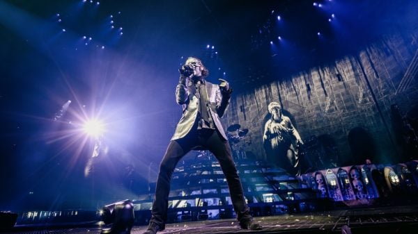Members of Ghost performing live on stage, wearing their signature costumes and masks, with dramatic lighting and stage effects.