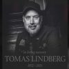 Black-and-white memorial portrait of Tomas Lindberg wearing a cap and jacket, seated on a staircase, with the text “In loving memory Tomas Lindberg 1972–2025.”