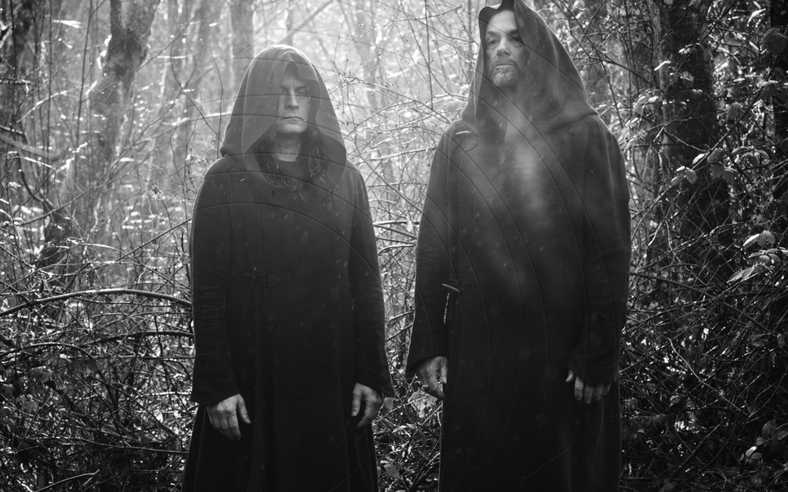 The two members of Sunn O))) standing side by side in black-and-white, wearing long robes, in a minimalist, dramatic composition.